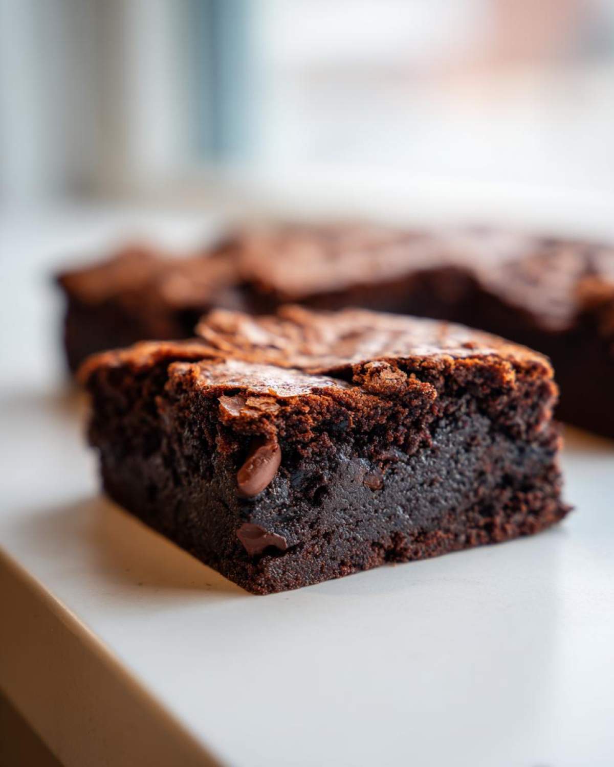 Close-up of a fudgy square of Brown Butter Brownies showing a shiny, crackly top and visible chocolate chips inside.