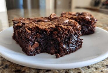 Two rich, fudgy brownie squares with a crackly top and visible chocolate chips served on a white plate.