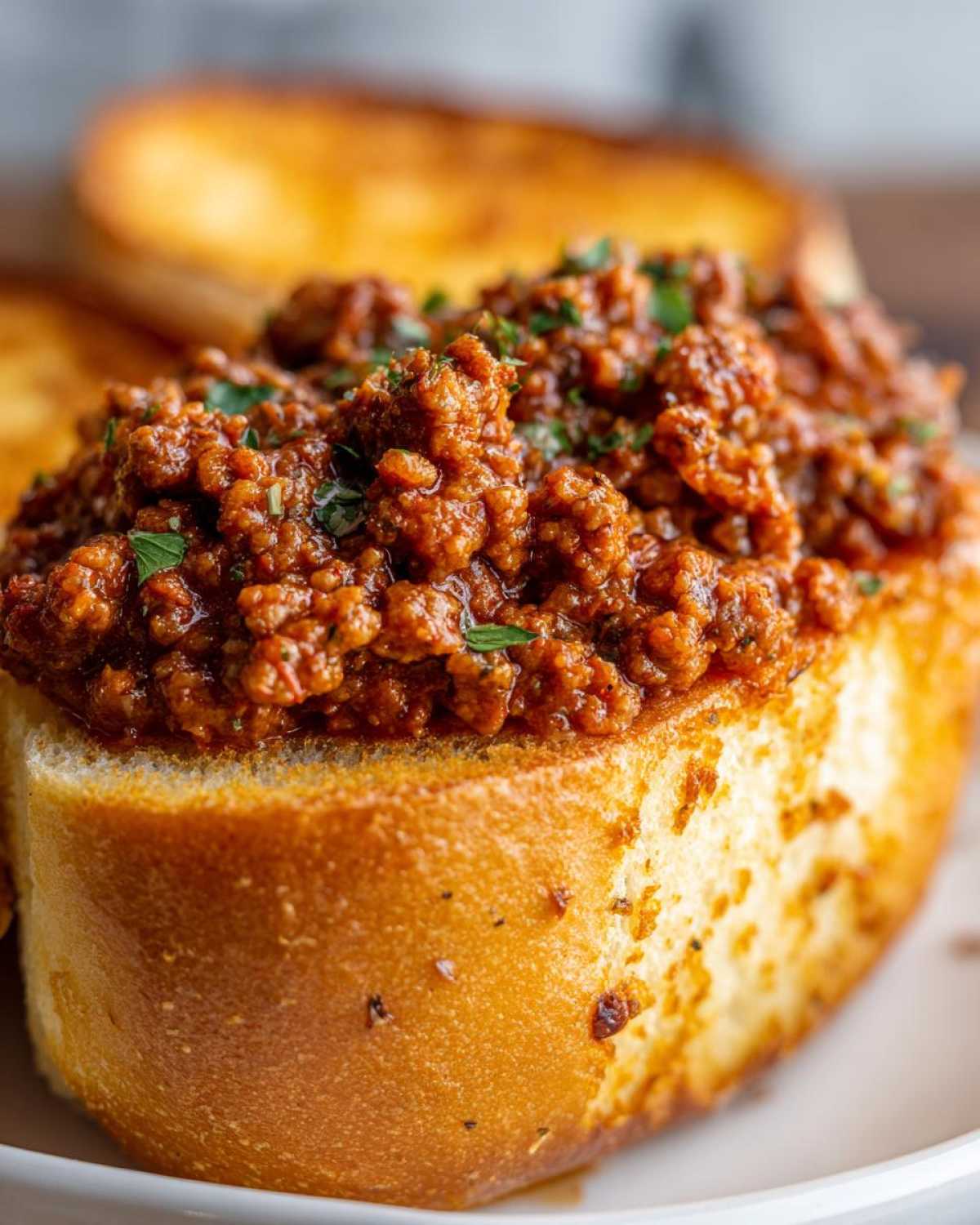 A close-up of rich, savory meat mixture served atop a slice of toasted garlic bread for Garlic Bread Sloppy Joes.