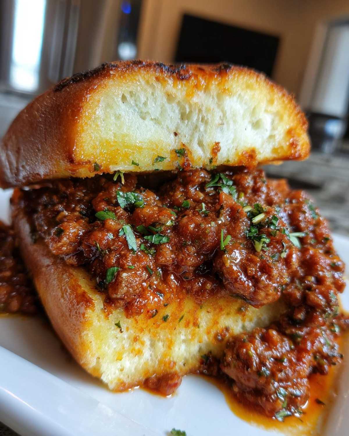 A close-up of a hearty portion of saucy meat filling piled high on toasted garlic bread for Garlic Bread Sloppy Joes.