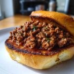A close-up of a hearty serving of saucy meat filling piled onto a toasted, buttery bun for Garlic Bread Sloppy Joes.