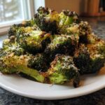 A mound of roasted Garlic Parmesan Broccoli florets sprinkled with grated cheese, served on a white plate.