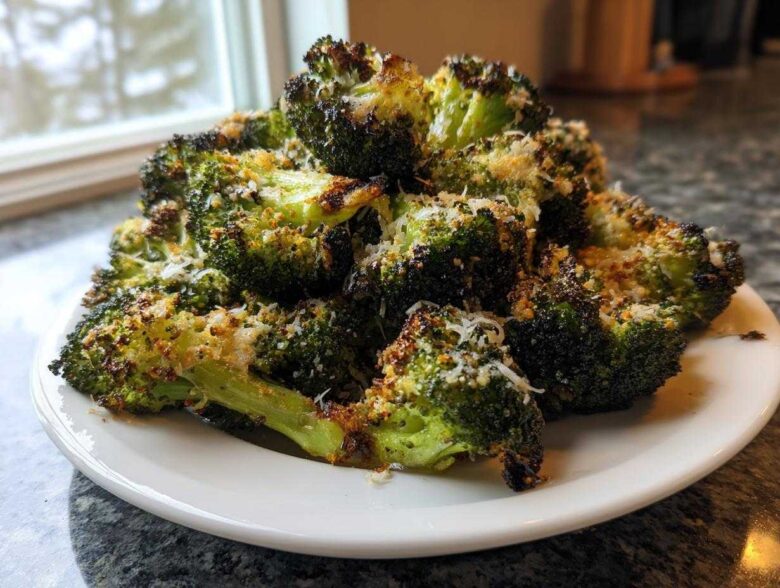 A mound of roasted Garlic Parmesan Broccoli florets sprinkled with grated cheese, served on a white plate.