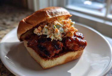 A delicious Gochujang Chicken Burger featuring glazed chicken and creamy slaw on a brioche bun, served on a white plate.