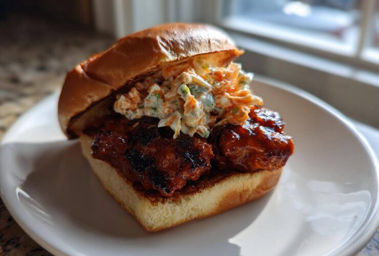 A delicious Gochujang Chicken Burger featuring glazed chicken and creamy slaw on a brioche bun, served on a white plate.