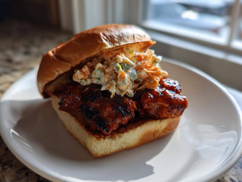 A delicious Gochujang Chicken Burger featuring glazed chicken and creamy slaw on a brioche bun, served on a white plate.