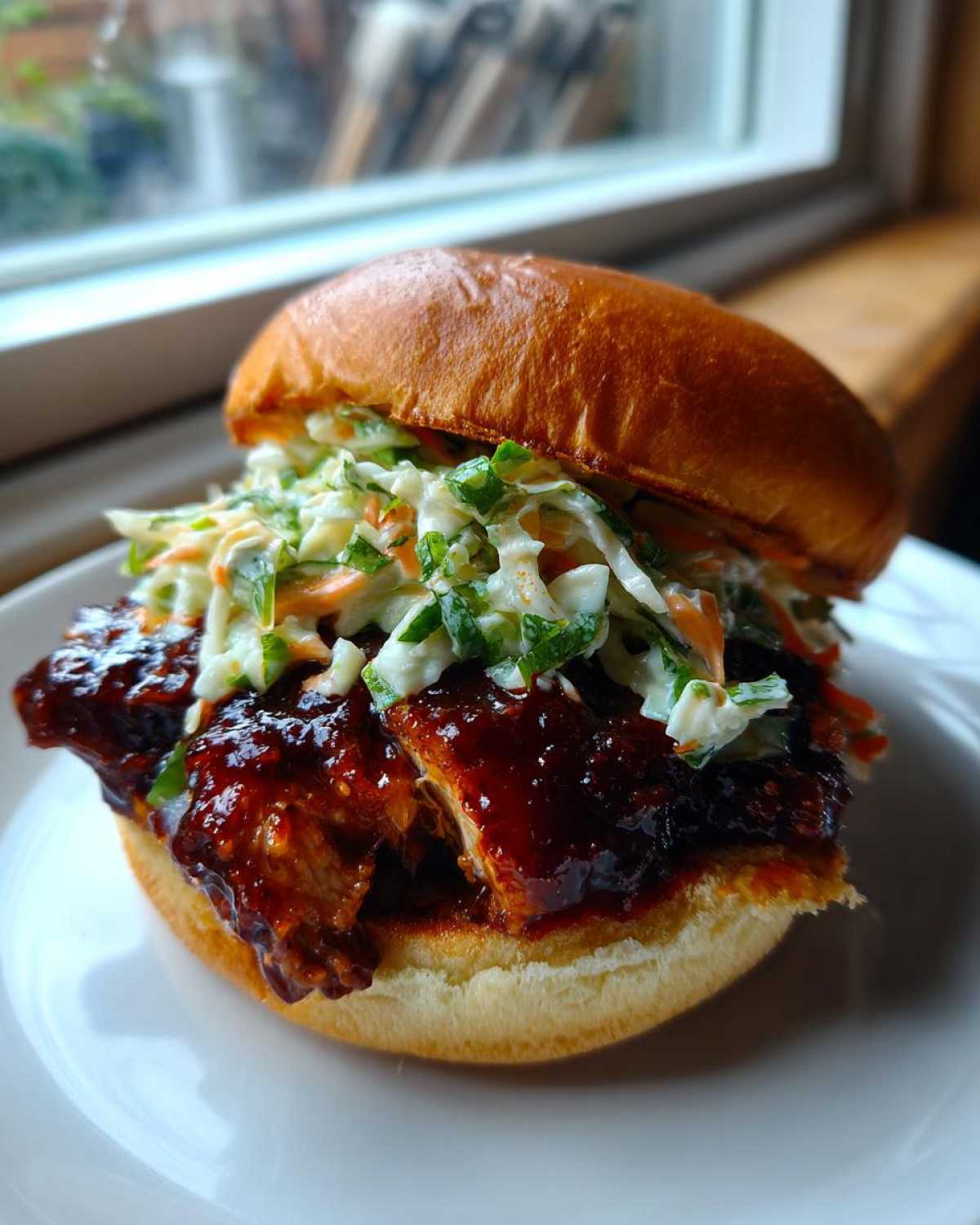 A close-up of a juicy Gochujang Chicken Burger topped with creamy coleslaw, served on a brioche bun.