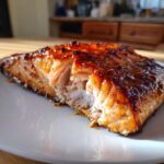 A close-up of a flaky, perfectly cooked piece of Grilled Honey Mustard Salmon with a caramelized, glossy glaze.