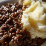Close-up of a serving of Hearty Lentil Stew with Creamy Mashed Potatoes on a white plate.