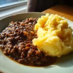 A close-up of Hearty Lentil Stew with Creamy Mashed Potatoes served in a light green bowl.