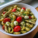 A bowl of High Protein Caprese Pasta Salad featuring orecchiette pasta, cherry tomatoes, mozzarella balls, and sliced chicken coated in pesto.