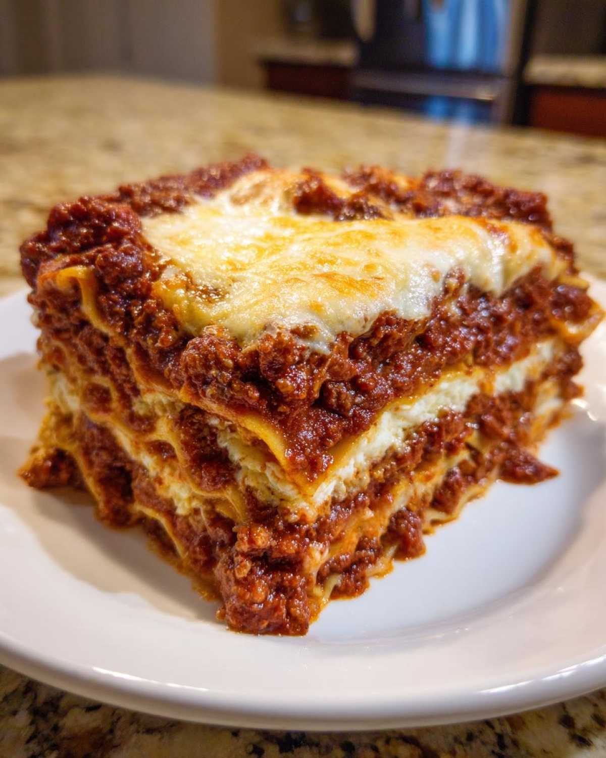 A generous slice of Homemade Classic Beef Lasagna showing multiple layers of pasta, rich meat sauce, and melted mozzarella cheese on top.