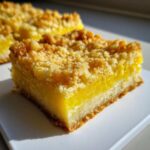 A close-up, bright photo of a square piece of Homemade Lemon Crumb Bars showing the thick, bright yellow filling and golden crumb topping.