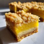 A close-up, featured shot of a square of Homemade Lemon Crumb Bars showing the thick, bright yellow filling and crumbly topping.