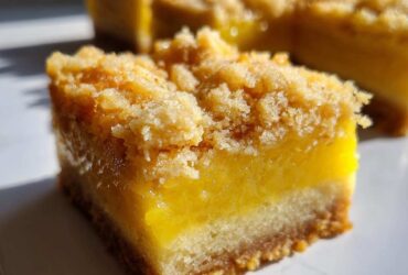 A close-up, featured shot of a square of Homemade Lemon Crumb Bars showing the thick, bright yellow filling and crumbly topping.