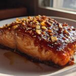 Close-up of a perfectly cooked salmon fillet covered in a thick, glossy Honey Garlic Glazed Salmon sauce, topped with sesame seeds and chopped nuts.