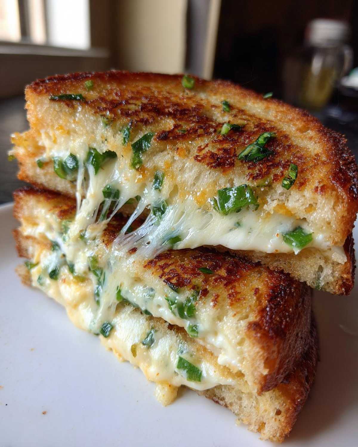 Close-up of a Jalapeño Popper Grilled Cheese Sandwich cut in half showing melted, stretchy cheese and green jalapeño pieces.