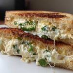 Close-up of a Jalapeño Popper Grilled Cheese Sandwich cut in half, showing gooey cheese and sliced jalapeños.
