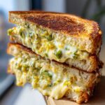 Close-up of a Jalapeño Popper Grilled Cheese Sandwich cut in half, showing gooey melted cheese and green jalapeño pieces.