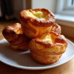 A stack of four golden-brown, puffed Jordan Pond Popovers resting on a small white plate.