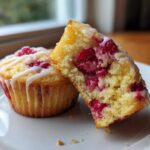A Lemon Raspberry Muffin cut in half showing the moist interior packed with raspberries, drizzled with white glaze.