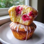 Two Lemon Raspberry Muffins stacked, the top one broken open to show moist interior and fresh raspberries.