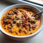 Close-up of a white bowl filled with rich, cheesy Loaded Cowboy Queso featuring ground beef, black beans, and diced red peppers.