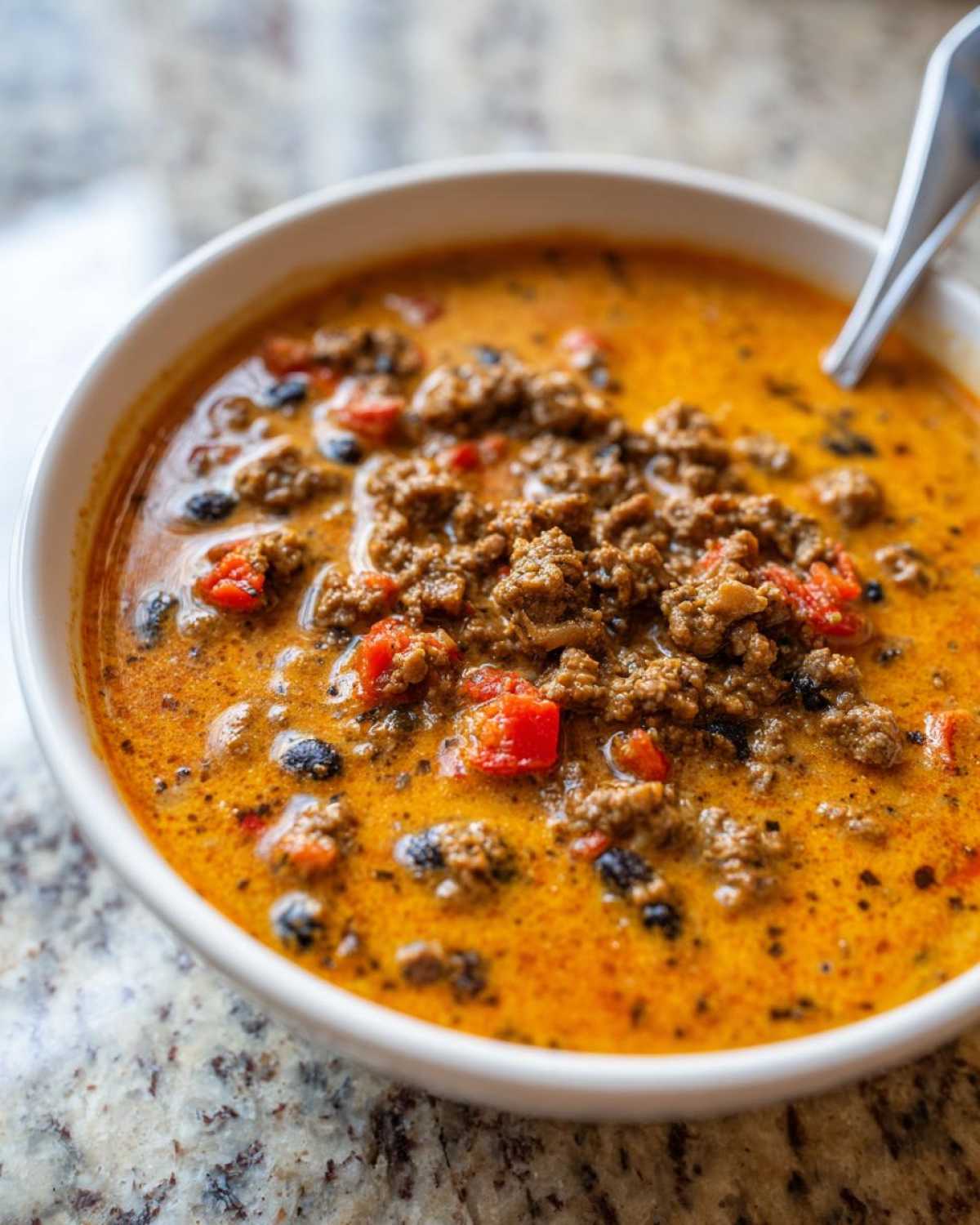 Close-up of a white bowl filled with creamy, orange Loaded Cowboy Queso topped with seasoned ground beef and diced tomatoes.