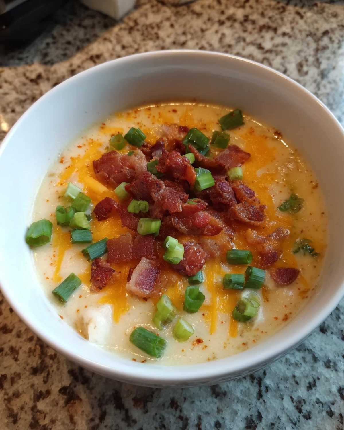 A close-up of a creamy bowl of Potato Soup topped with shredded cheese, bacon bits, and green onions.