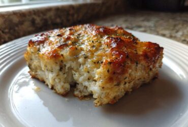 A close-up of a baked portion of Mayo Parmesan Cod showing the flaky white fish and browned, herbed cheese topping.