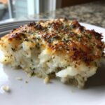 A close-up of a serving of flaky Mayo Parmesan Cod with a golden brown, herbed crust on a white plate.