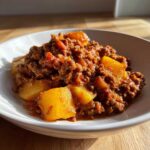 A close-up of Mexican Picadillo with Potatoes, featuring seasoned ground meat and chunks of yellow potato in a white bowl.