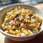 Close-up of creamy Mexican Street Corn Pasta Salad featuring corn, red onion, and cilantro in a white bowl.