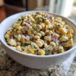 Close-up of creamy Mexican Street Corn Pasta Salad featuring elbow macaroni, corn, red onion, and cilantro in a white bowl.