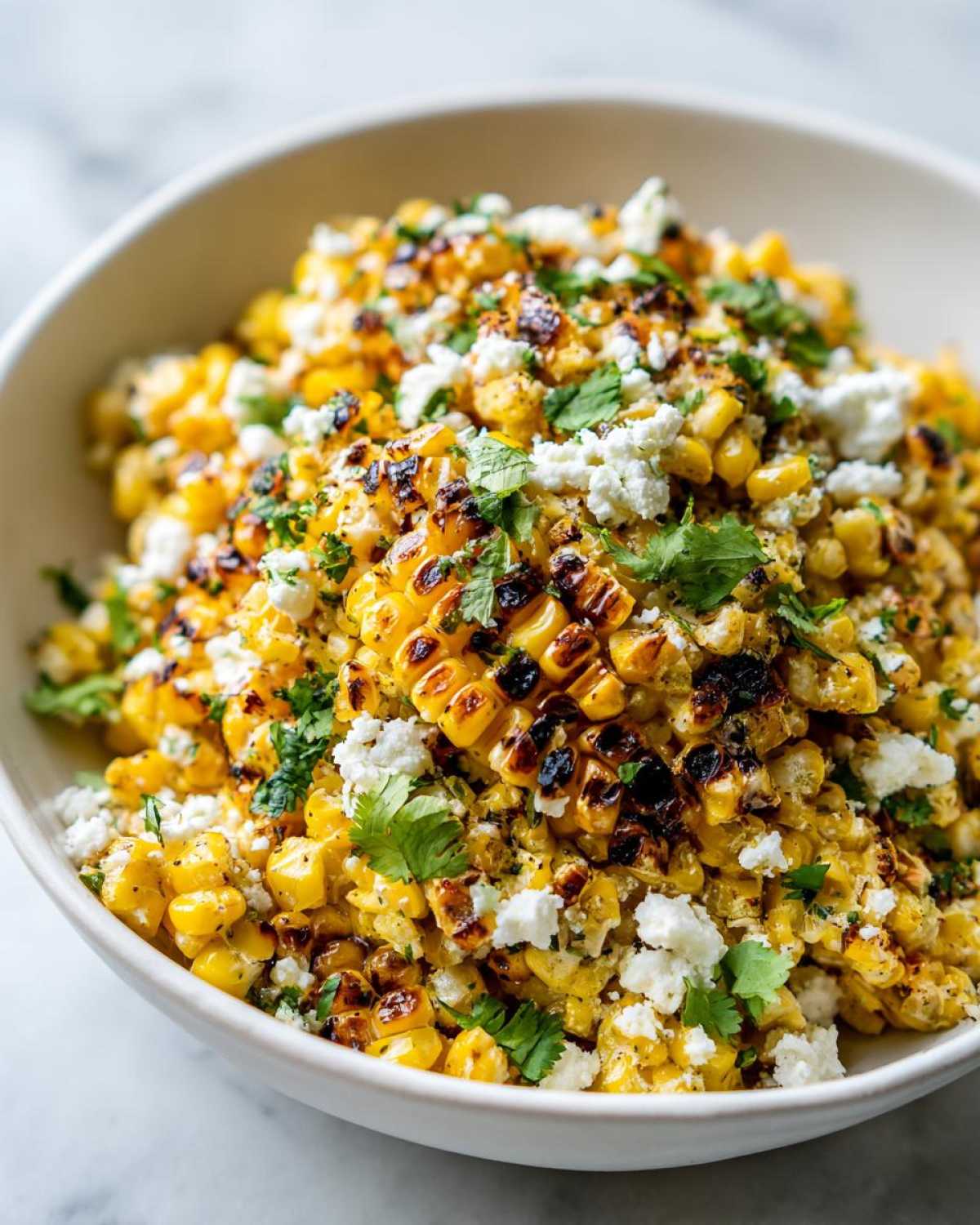 Close-up of grilled corn kernels mixed with cotija cheese and cilantro, ready to serve as Mexican Street Corn Salad Esquites.