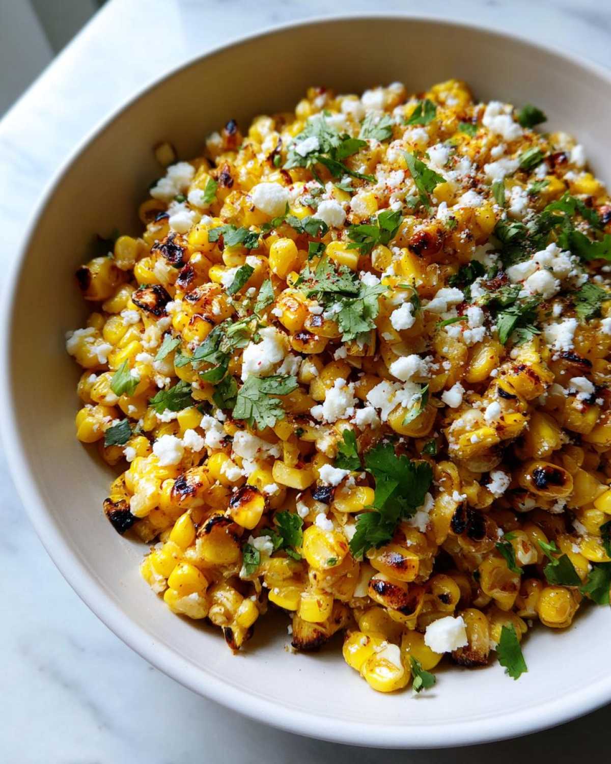 Close-up overhead view of Mexican Street Corn Salad Esquites featuring charred corn kernels, crumbled white cotija cheese, and fresh cilantro.