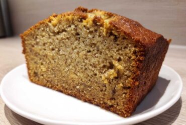 Close-up of a thick slice of moist Banana Bread showing a tender crumb and golden-brown crust, served on a white plate.