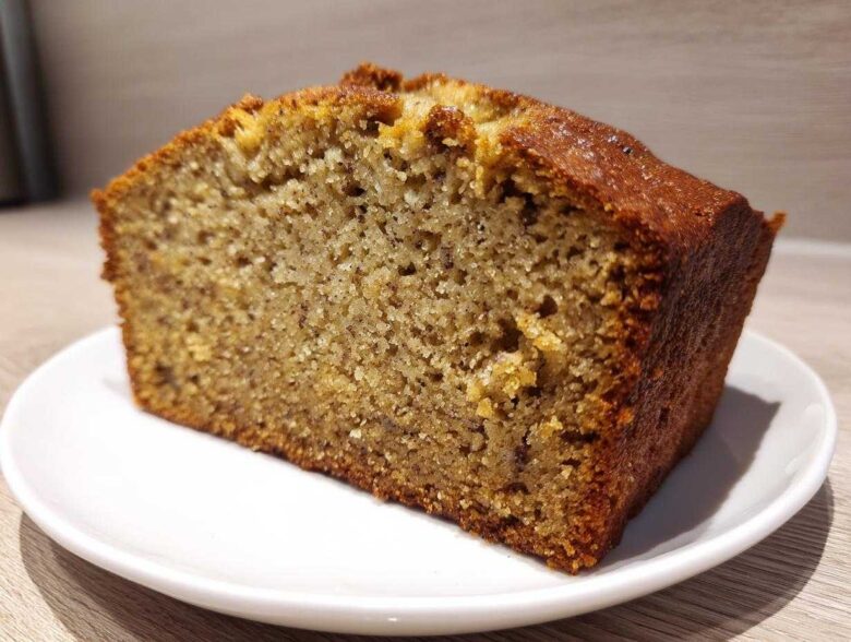 Close-up of a thick slice of moist Banana Bread showing a tender crumb and golden-brown crust, served on a white plate.