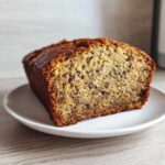 A close-up of a thick slice of moist Banana Bread showing the speckled interior and dark, caramelized crust.