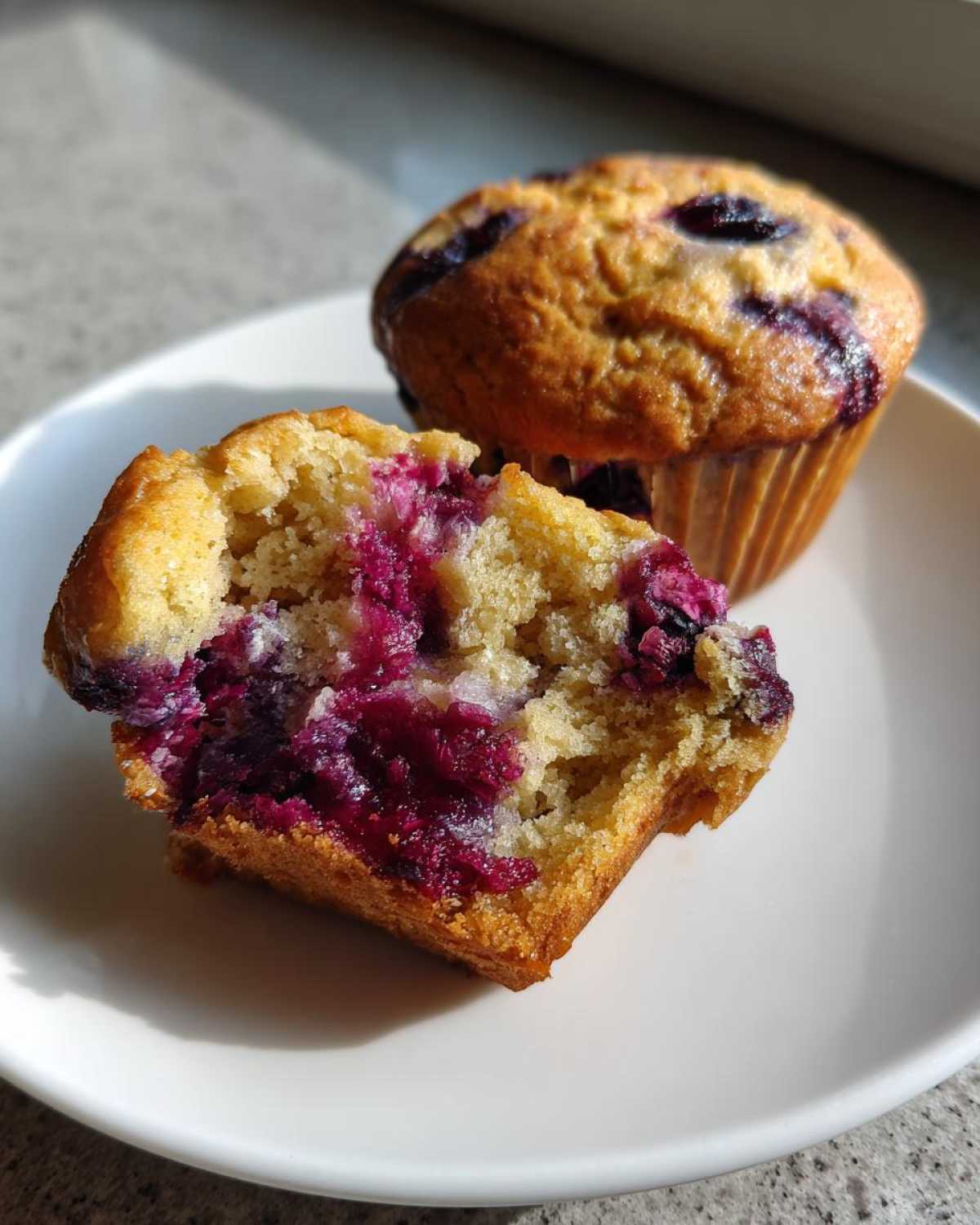 Close-up of a homemade Blueberry Muffins cut in half showing the moist, berry-filled interior next to a whole muffin.
