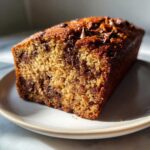 A close-up view of a freshly baked, moist Chocolate Chip Banana Bread loaf with a golden crust and visible chocolate chips.