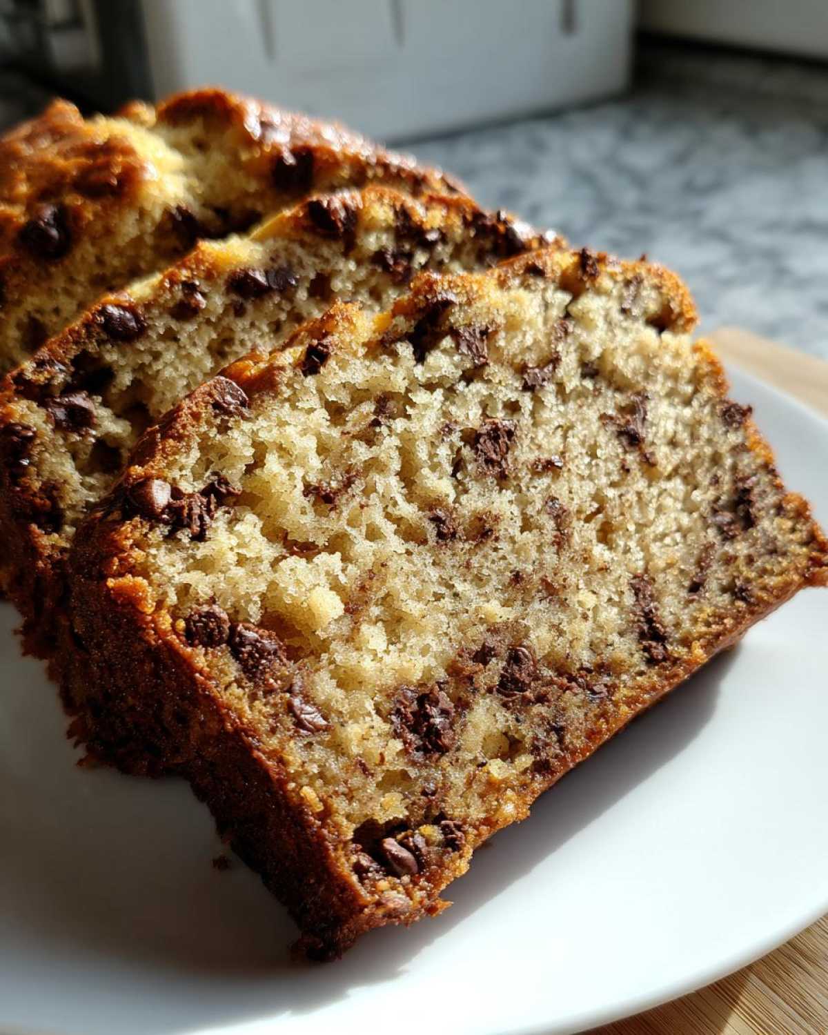 Close-up of three moist slices of Chocolate Chip Banana Bread stacked on a white plate.