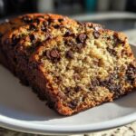 Close-up of thick slices of moist Chocolate Chip Banana Bread, studded with melted chocolate chips, sitting on a white plate.