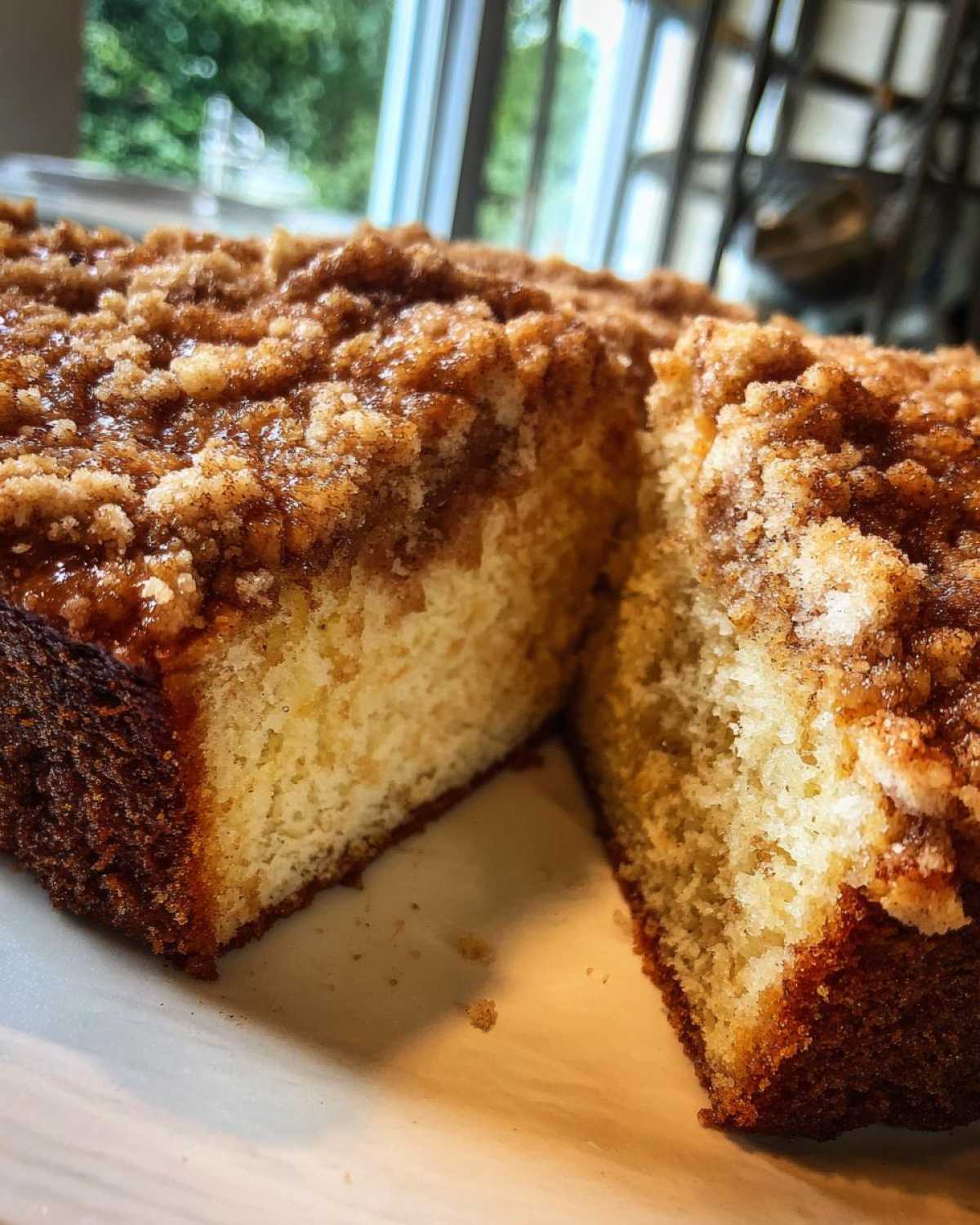 Close-up of a moist coffee cake cut in half, showing the tender crumb and thick, sugary cinnamon streusel topping.