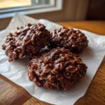 Three rich, dark No-Bake Chocolate Oat Cookies clustered together on a piece of white parchment paper.