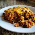 A close-up serving of One Pan Taco Quinoa Casserole topped with melted cheddar cheese on a white plate.