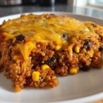 A close-up serving of One Pan Taco Quinoa Casserole with visible quinoa, black beans, corn, and melted cheddar cheese on top.