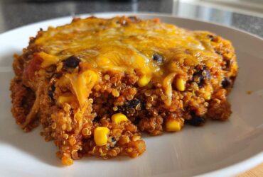 A close-up serving of One Pan Taco Quinoa Casserole with visible quinoa, black beans, corn, and melted cheddar cheese on top.
