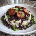 A serving of One-Pot Black Beans and Rice with Sausage, topped with seared sausage rounds and fresh cilantro.