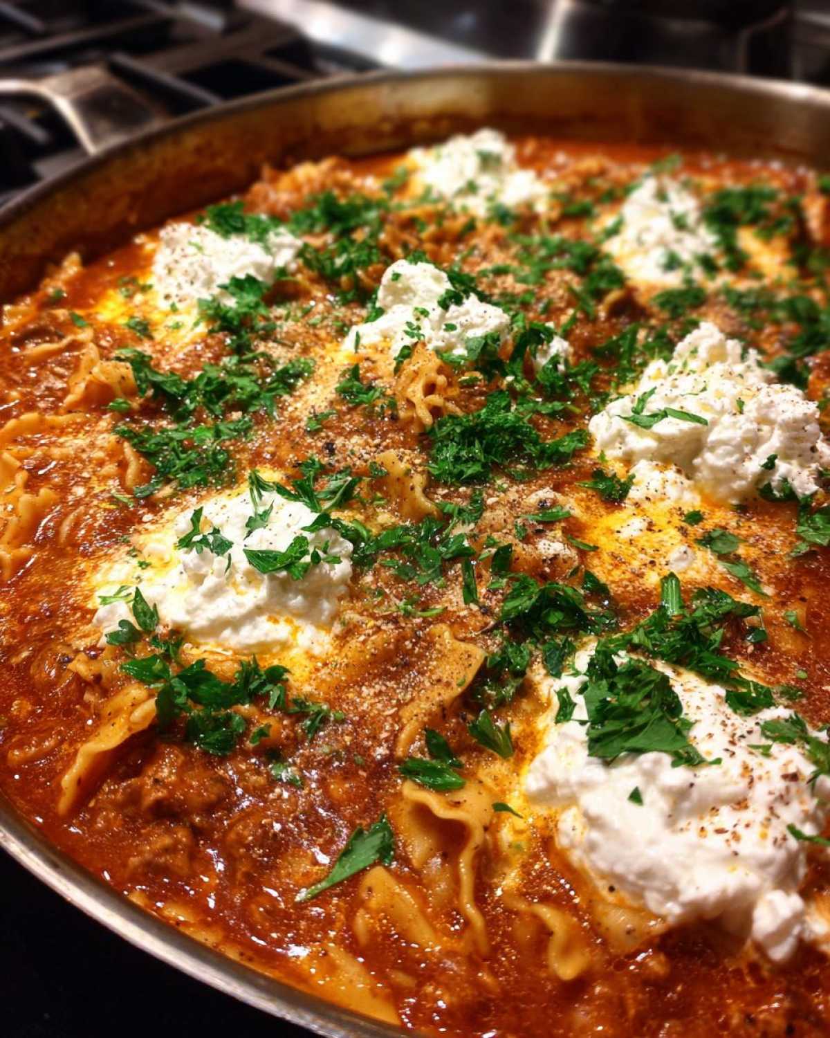 Close-up of rich, tomato-based Lasagna Soup in a skillet, topped with dollops of ricotta cheese, fresh parsley, and Parmesan.